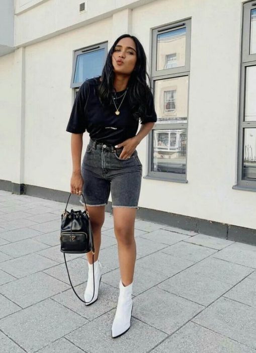 Chica usando bermudas de mezclilla con blusa de color negro y botines blancos 