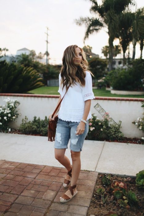 Chica usando bermudas de mezclilla con blusa de color blanco y sandalias 