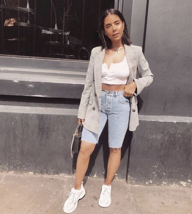 Chica usando bermudas de mezclilla con top de color blanco y tenis de color blanco 