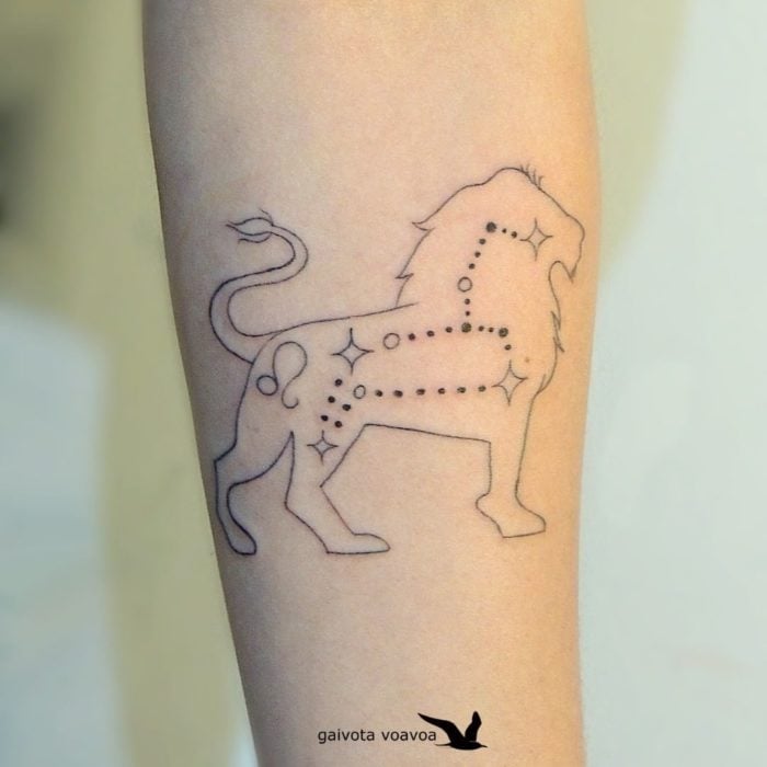 Tatuaje de la constelación de leo con la silueta de un león rodeándola en el área del antebrazo