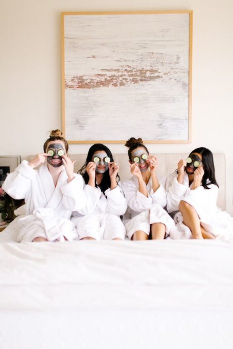 Grupo de amigas recostadas en una cama usando mascarillas con rodajas de pepino