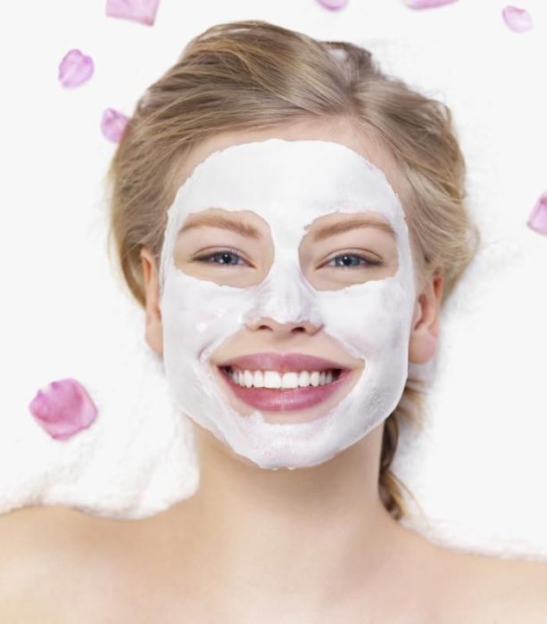 Chica sonriendo mientras tiene aplicada una mascarilla en el rostro