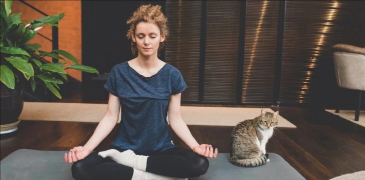 Chica meditando en casa en compañía de su gato