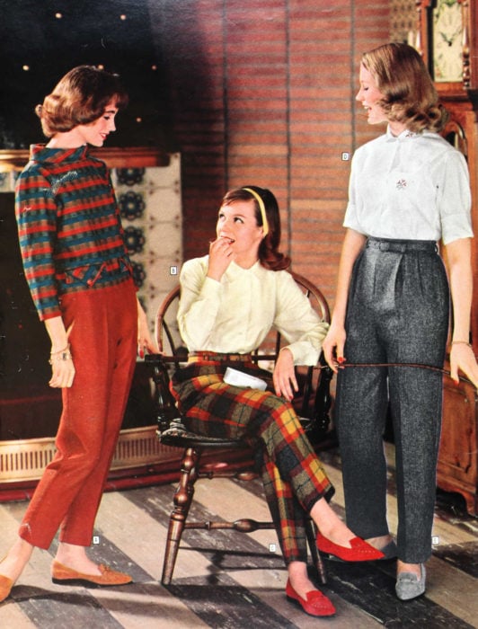 Moda femenina de los 70; tres amigas hablando y riendo; pantalón gris, de ciadros rojos y amarillos, blusa blanca y abrigo de patrones, flats anaranjados y grises; ropa y peinado retro