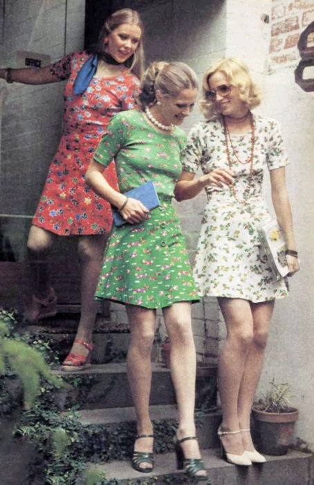 Moda femenina de los 70; amigas bajando escaleras, vestidos florales arriba de la rodilla, rojo, blanco y verde, con sandalias; ropa y peinados retro