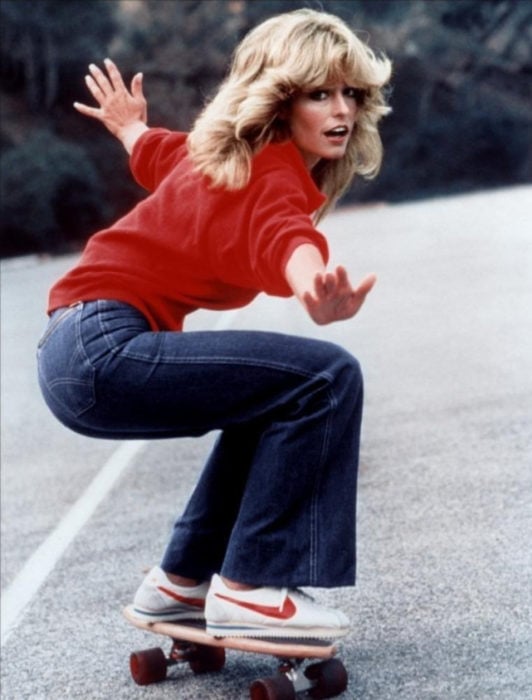 Moda femenina de los 70; Farrah Fawcett en patineta con suéter rojo; peinado retro