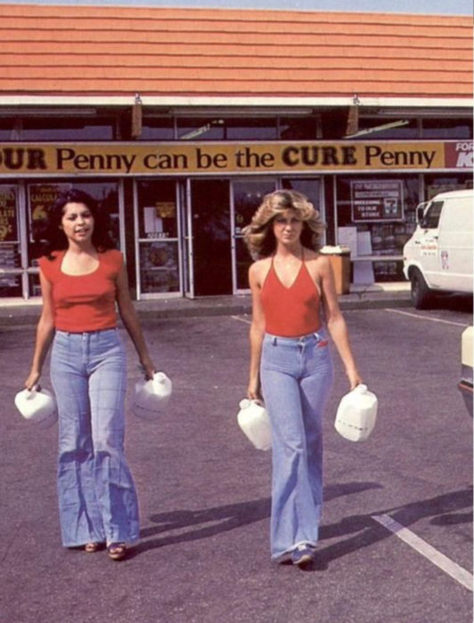 Moda femenina de los 70; mujeres amigas en estacionamiento saliendo de la tienda, con jeans acampanados y blusa roja; ropa y peinados retro