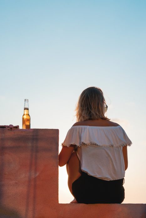 Chica sentada de espaldas y una cerveza en la barrita