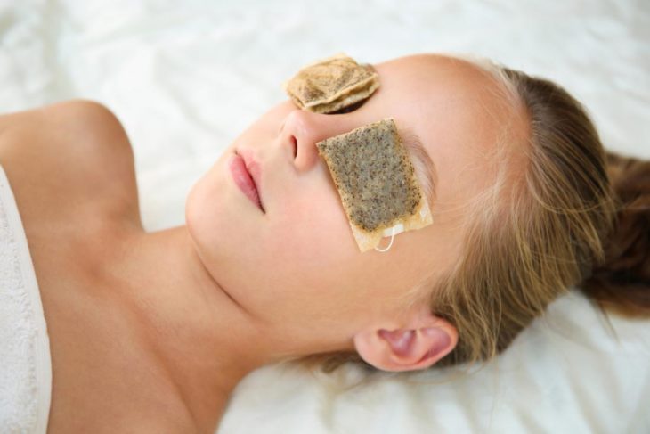 Chica con bolsas de té en los ojos para evitar el efecto de ojos cansados