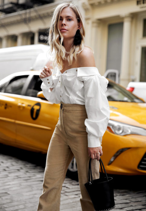 Outfit con blusa blanca; mujer rubia en la calle esperando taxi, con camisa sin hombros