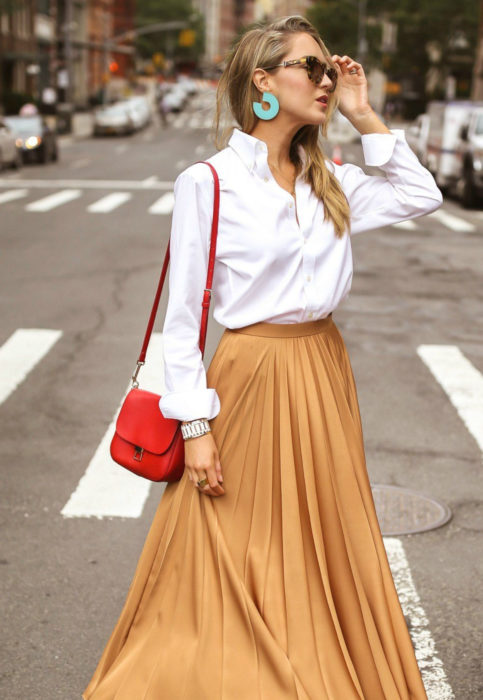 Outfit con blusa blanca; mujer rubia con lentes de sol, aretes grandes, camisa y falda anaranjada 