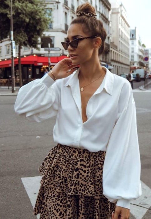 Outfit con blusa blanca; mujer en la calle, estilo retro, lentes triangulares, chongo alto, falda de animal print