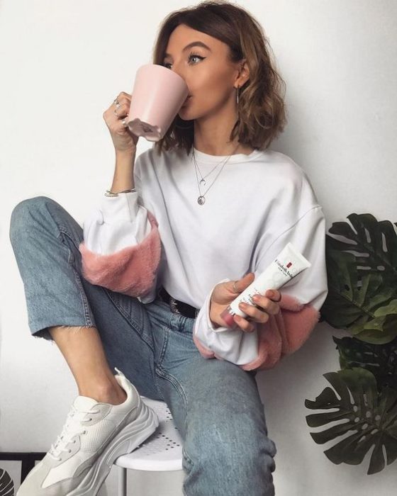 Chica de cabello corto viste una sudadera blanca con rosa y jeans