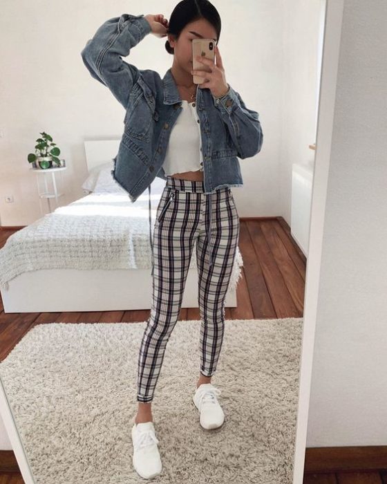 Chica se toma selfie frente al espejo con pantalín a cuadros, blusa blanca y chaqueta de mezclilla