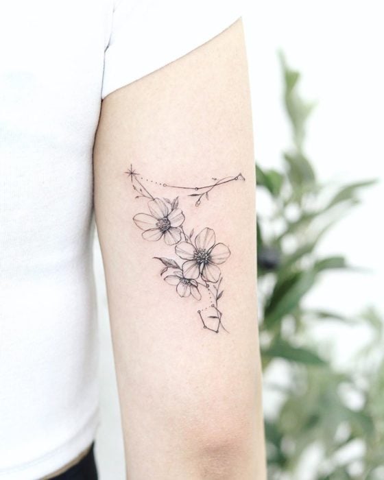 Tatuaje de la constelación de piscis sobre la parte trasera del brazo adornada con flores a tinta negra