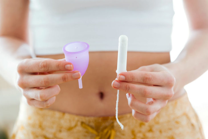 Chica sosteniendo un tampon y copa menstrual