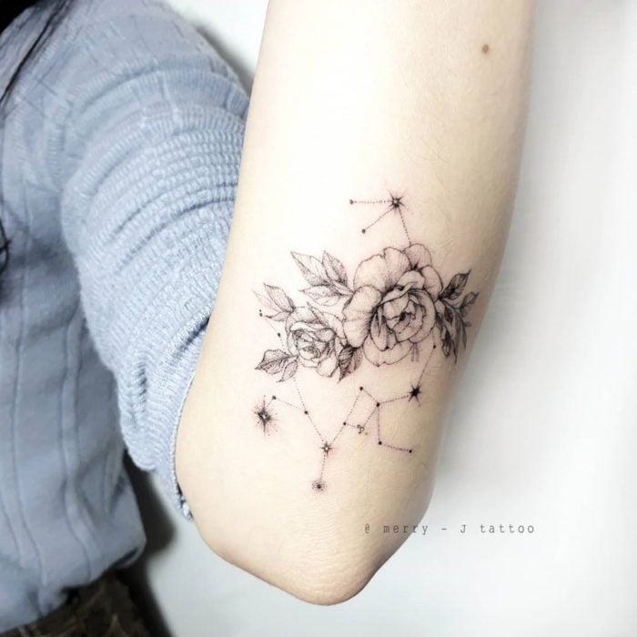 Tatuaje de la constelación de sagitario adornada con flores, en el área trasera del antebrazo en tinta negra