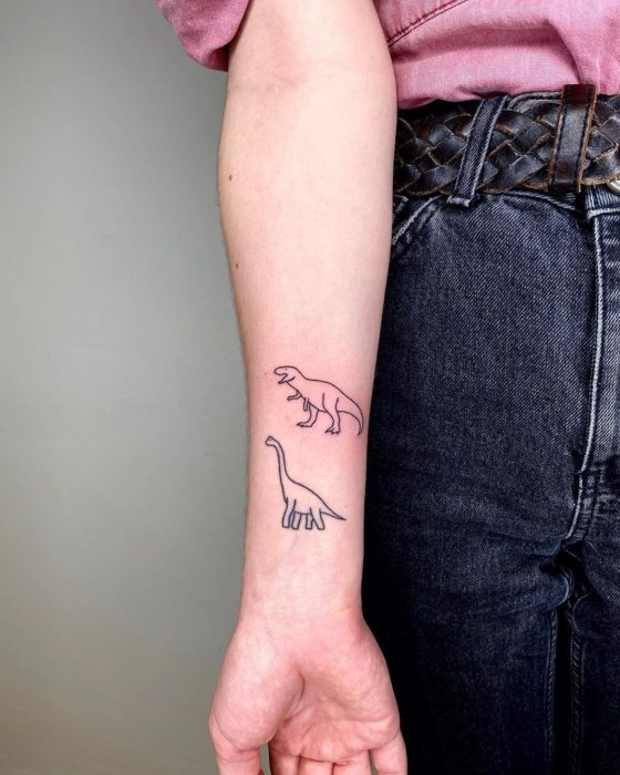 Tatuaje al estilo hand poke de dos dinosaurios