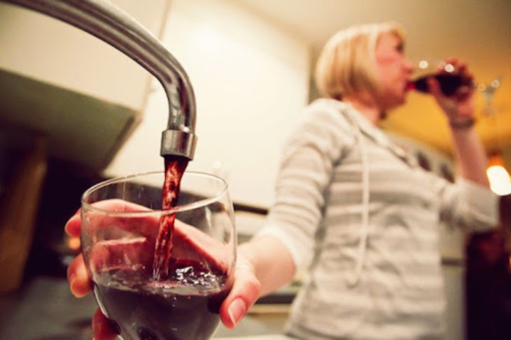 Mujer tomando vino que sale del grifo de su casa