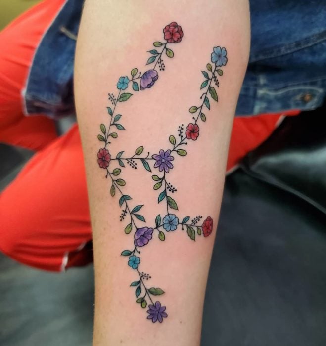 Tatuaje de la constelación de virgo hecha con flores y a color en el área del antebrazo