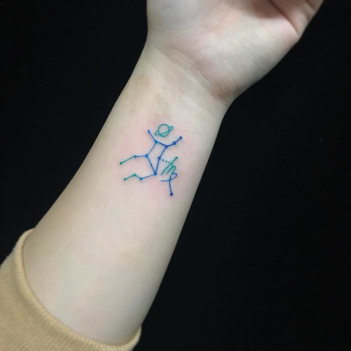 Tatuaje de la constelación de virgo con tinta azul en el área de la muñeca