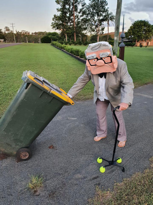 Señor disfrazado de anciano de Up mientras saca la basura 