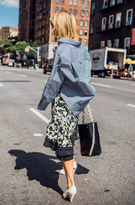 Atuendos con tu boyfriend shirt, camisa de tu novio, blusa oversized azul con rayas, falda con ornamentos, tacones blancos, mujer rubia caminando en la calle