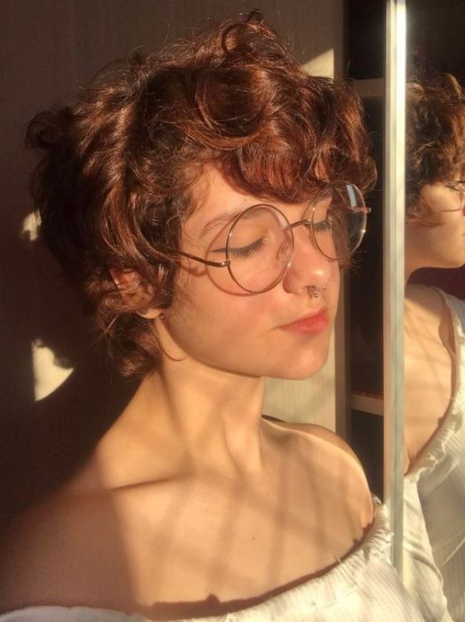 Chica pelirroja con cabello rizado y muy corto con lentes grandes redondos