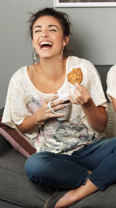 Chica riendo a arcajadas mientras come una galleta y toma un té