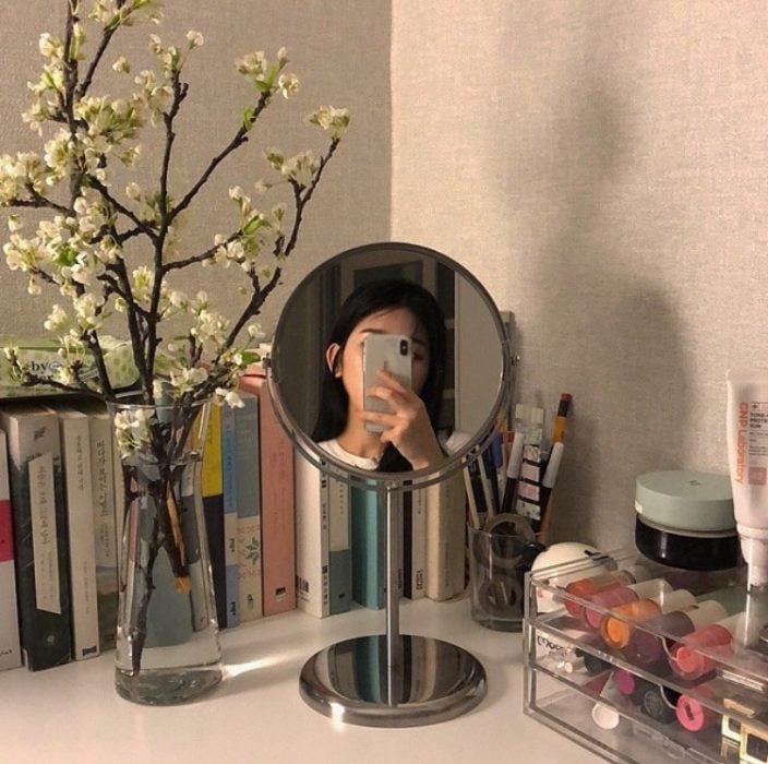 Chica se toma selfie frente a espejito redondo en un escritorio