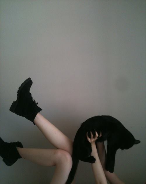 Chica acostada levanta sus piernas y carga a su gato negro en brazos