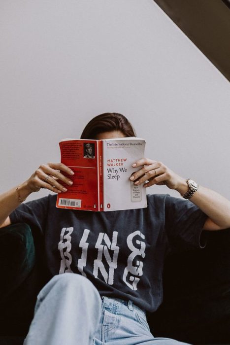 Chica con blusa negra sostiene un libro y se tapa la cara