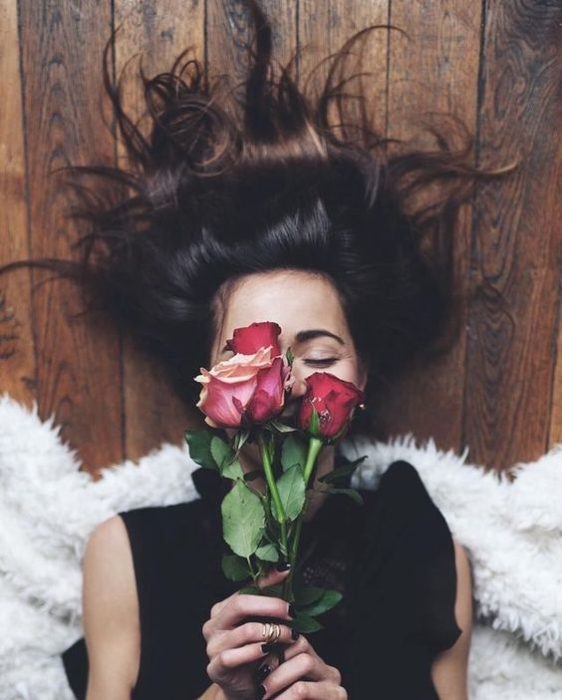 Chica acostada en el piso con el cabello extendido y flores en la casa