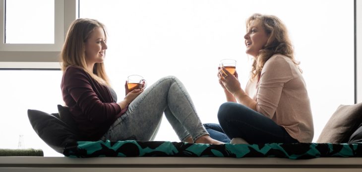 Madre e hija bebiendo te mientras están sentadas en la ventana 