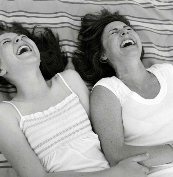 Madre e hija riendo mientras están recostadas en el pasto 