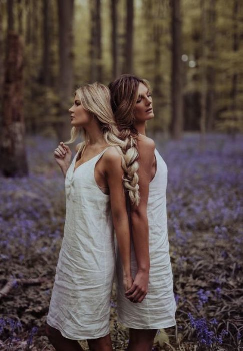 Madre e hija unen su cabello largo en una trenza en un bosque lleno de flores moradas