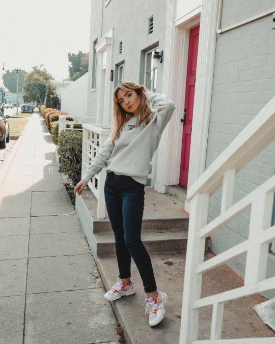 Chica usando unos skinny jeans con sueter de color blanco y tenis