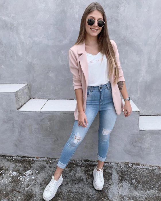 Chica usando unos skinny jeans, tenis blancos, blazer rosa y camisa blanca 