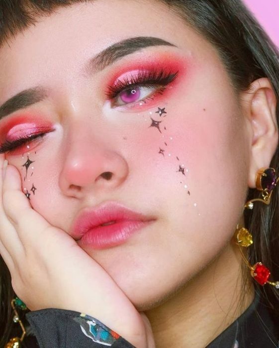 Chica con maquillaje de ojos rosa con rojo y estrellitas en la cara