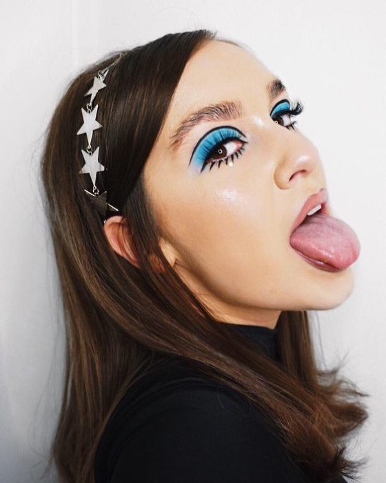 Chica con sombra azul y diadema de estrellas saca la lengua