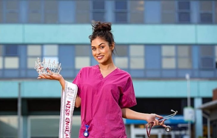 Bhasha Mukherjee vistiendo su uniforme de médico y con su corona y banda de Miss Inglaterra