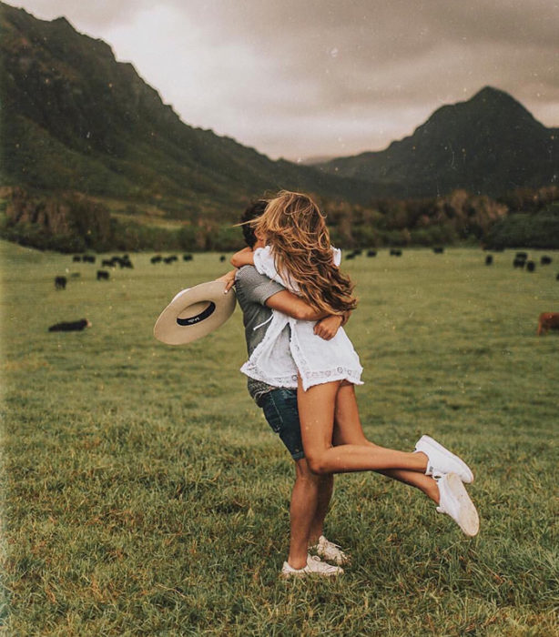 Hombre carga a su novia en brazos mientras dan vueltas en un campo verde y hermoso
