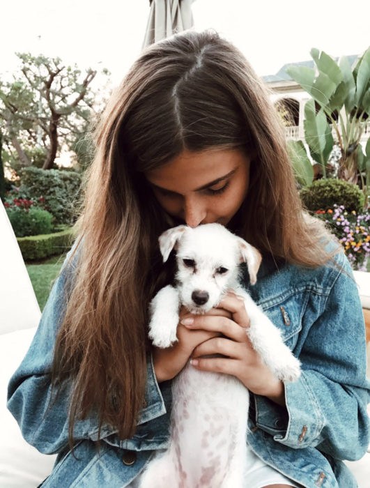 Mujer cargando a perrito blanco y dándole un beso