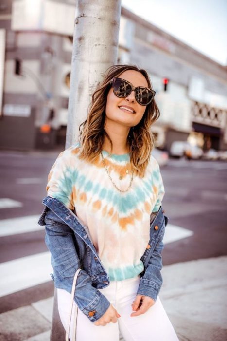 Chica con cabello suelto y lentes usa chaqueta de mezclilla y blusa con efecto deslavado o tie dye