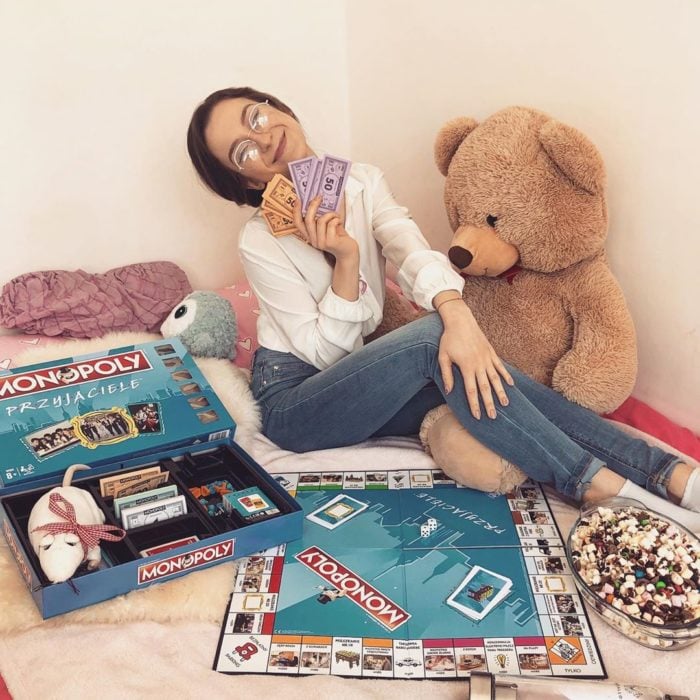 Chica sentada frente a un tablero de monopoly jugando 