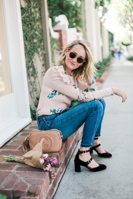 Chica rubia viste pantalón de mezclilla, blusa rosa de flores y zapatos de tacón cuadrado