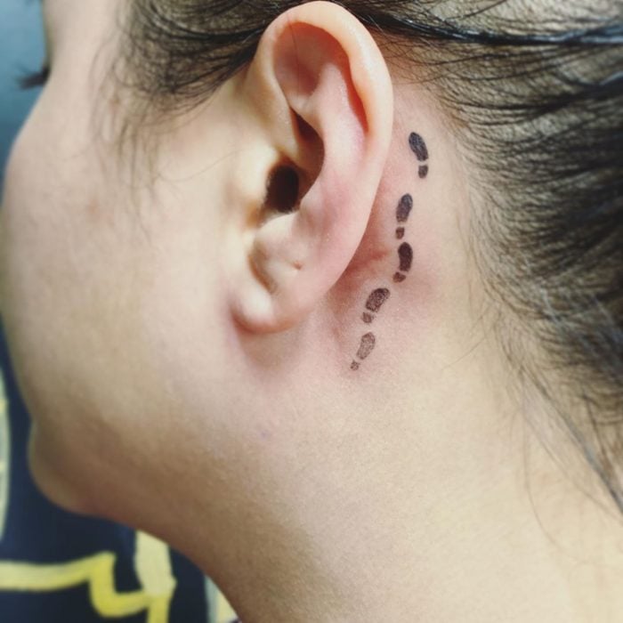 Tatuaje detrás de la oreja de huellas de pies