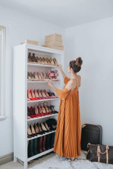 Mujer con vestido naranja acomoda zapatos en una mueble blanco 