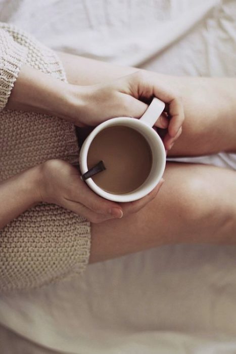 Chica sosteniendo una taza de café entre las piernas