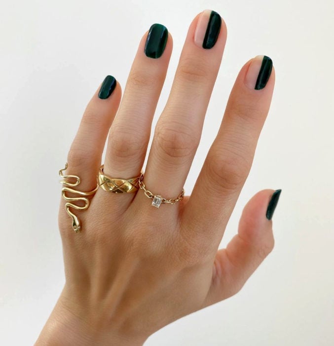 Diseños de uñas sencillos para hacer en casa; esmale verde oscuro, líneas verticales, mano con anillos dorados de serpiente